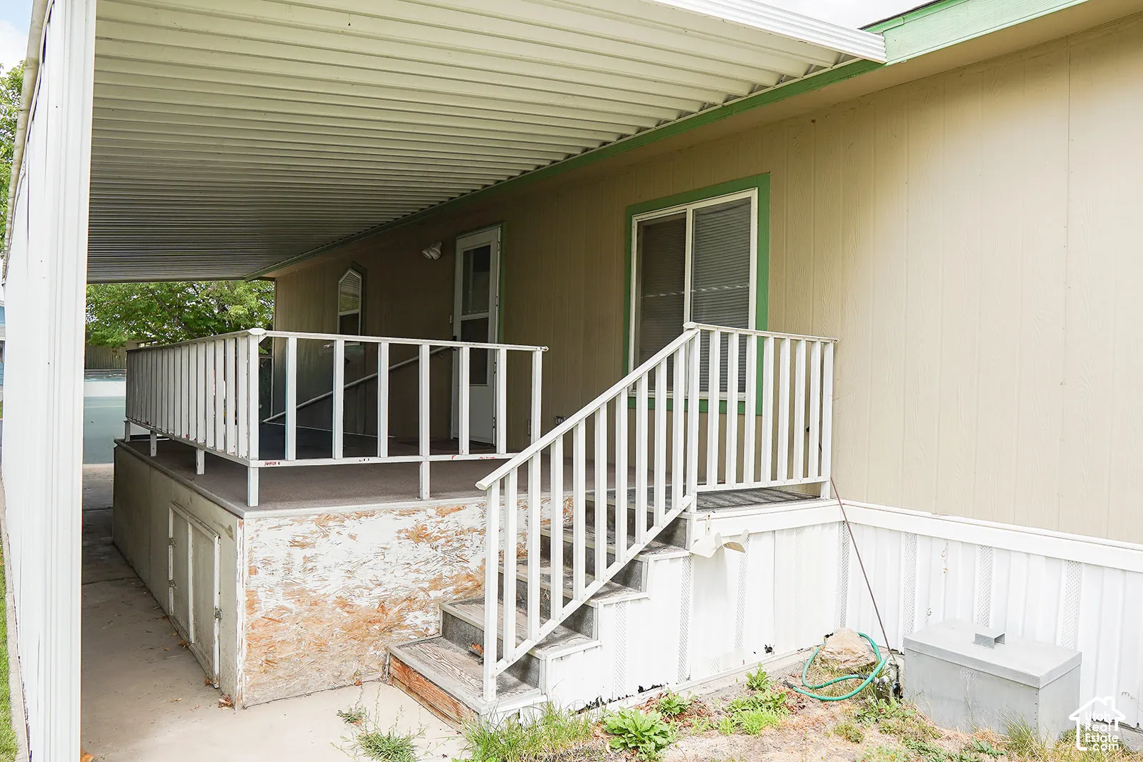 Covered entry featuring a white aluminum railing system, concrete foundation with stone veneer accents, and a metal roof overhang