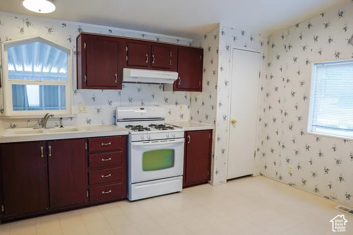 Kitchen featuring wood-finish cabinetry, white laminate countertops, and a white gas range with overhead ventilation