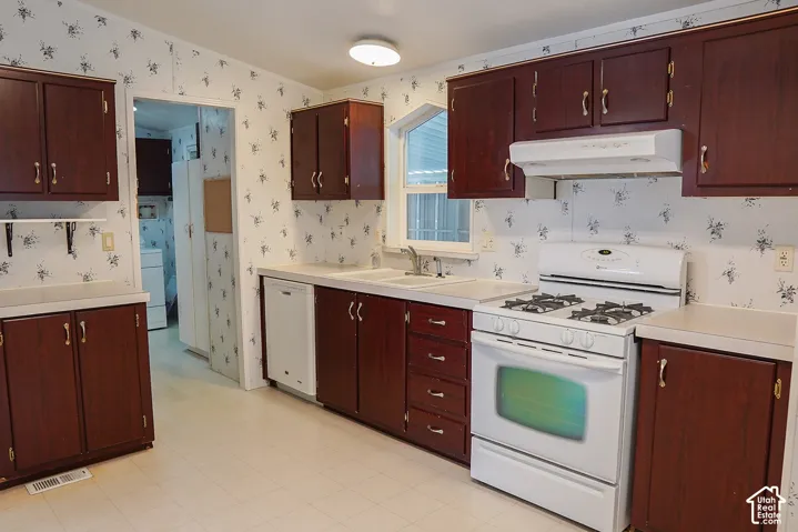Kitchen featuring wood-finish cabinetry, white countertops, a white gas range, a white dishwasher, and a double basin sink