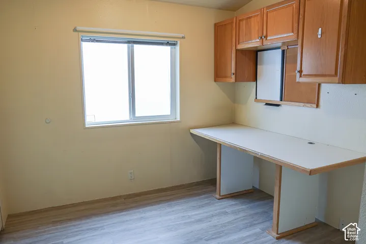 Built-in desk with overhead cabinetry, a sliding window, and wood-finish flooring