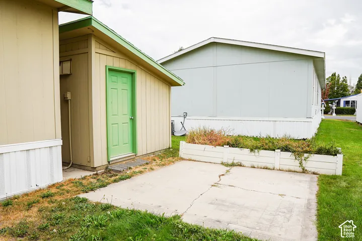 Outdoor storage structure with a green door, concrete pad, and an adjacent planted garden bed
