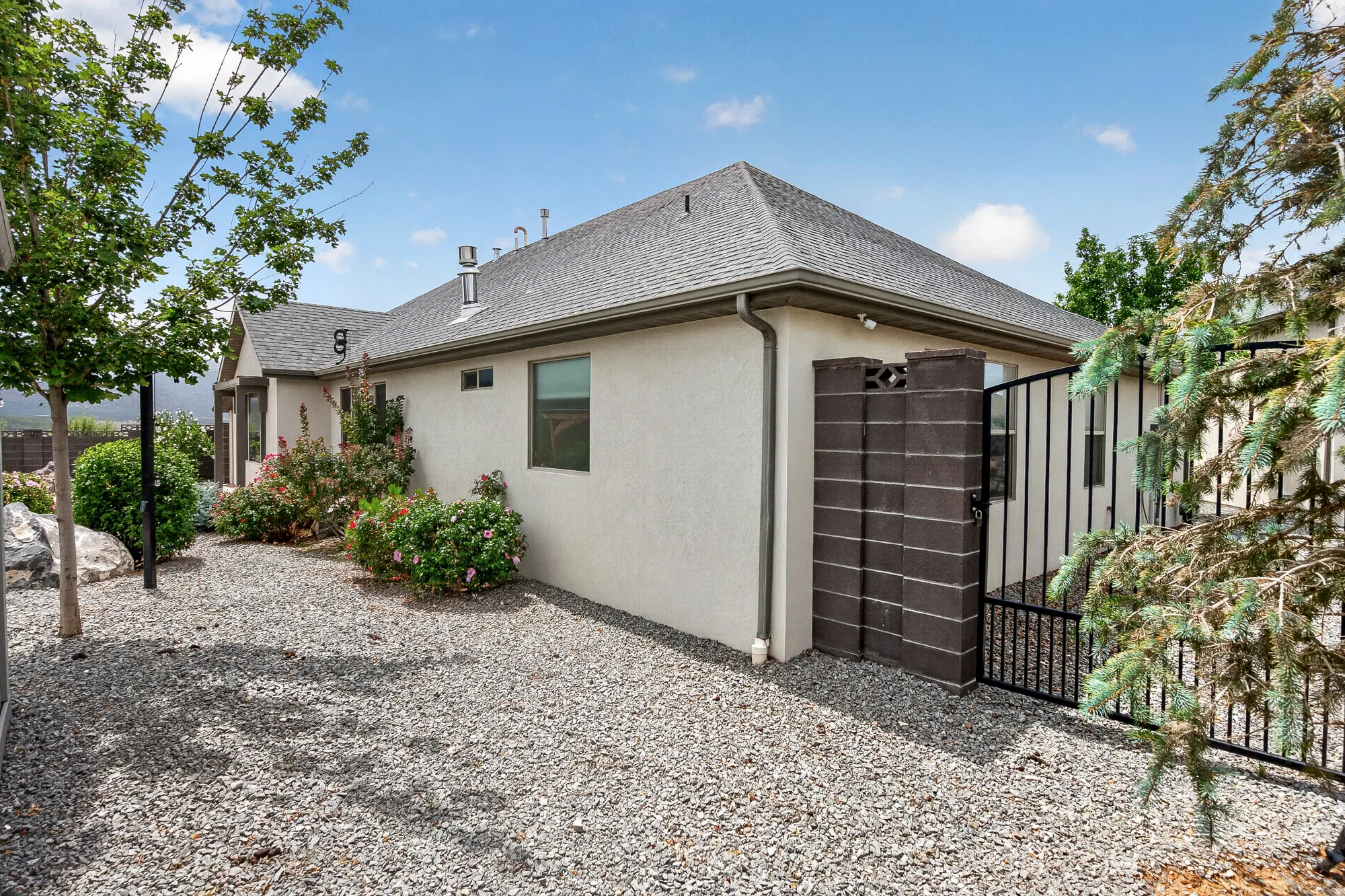 Modern residence featuring a clean stucco exterior with a pitched roof, dark wood-finish garage door with metal framing, and a gravel driveway bordered by mature landscaping