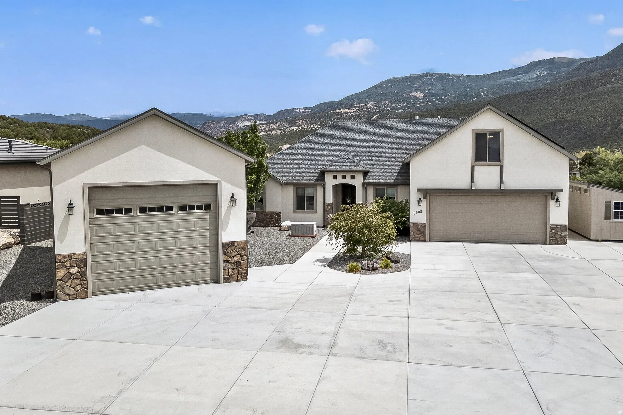 Modern residence showcasing a spacious concrete driveway with dual garage bays, crisp white exterior with peaked rooflines, and mountain backdrop