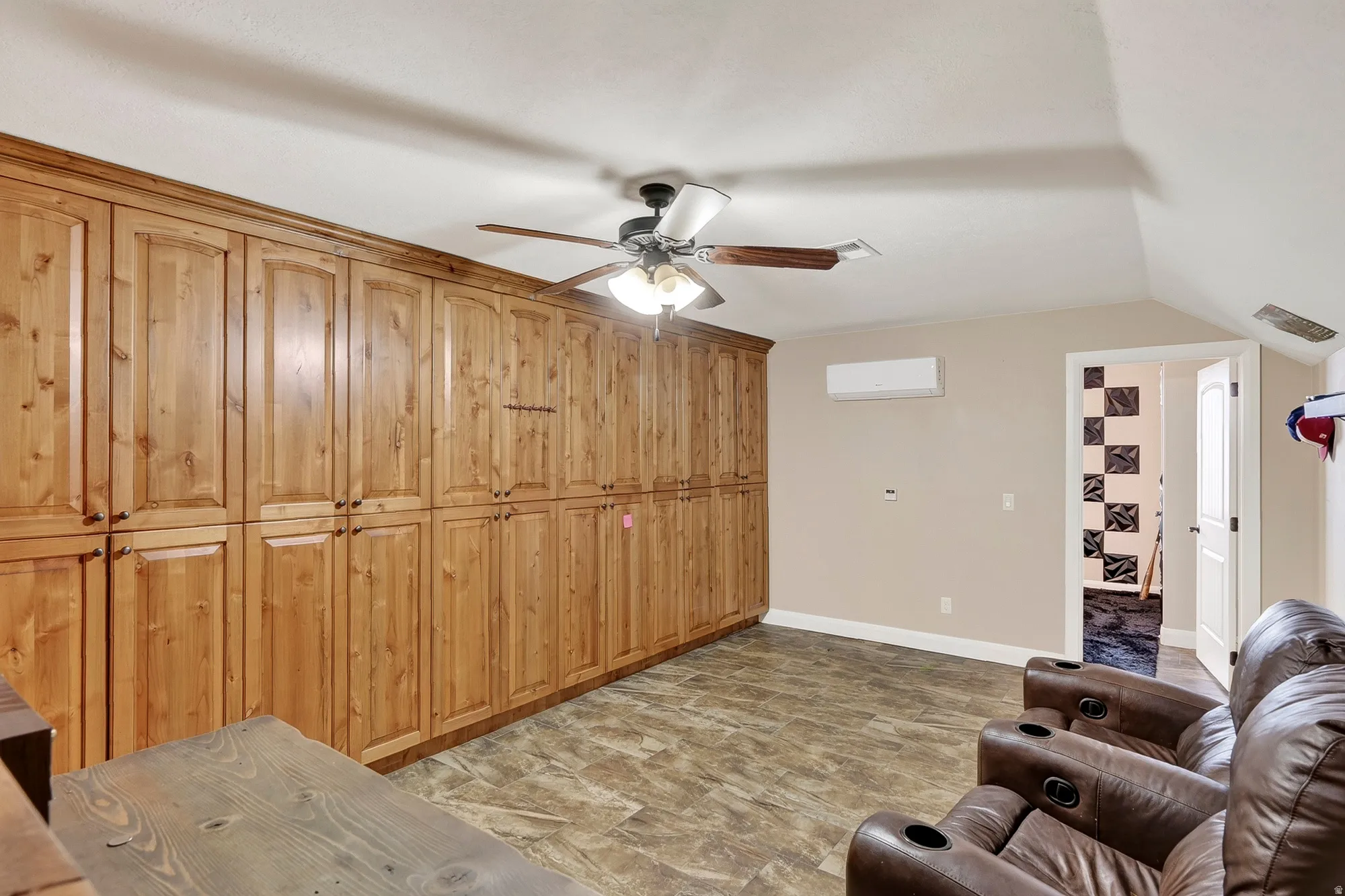 Spacious primary suite featuring extensive wood cabinetry with vertical paneling, ceiling fan with integrated lighting, and neutral carpeting throughout