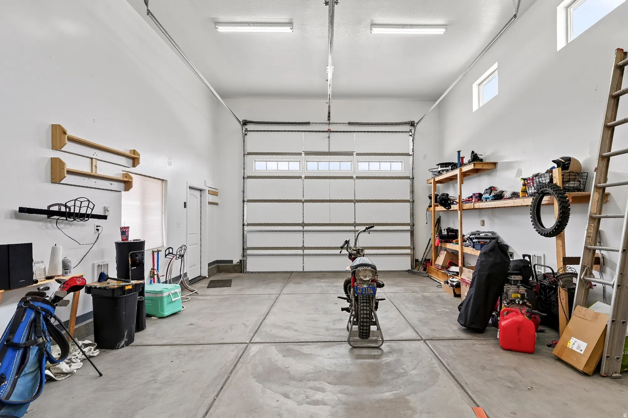 Spacious garage with concrete flooring, overhead fluorescent lighting, and a white paneled garage door with upper window inserts