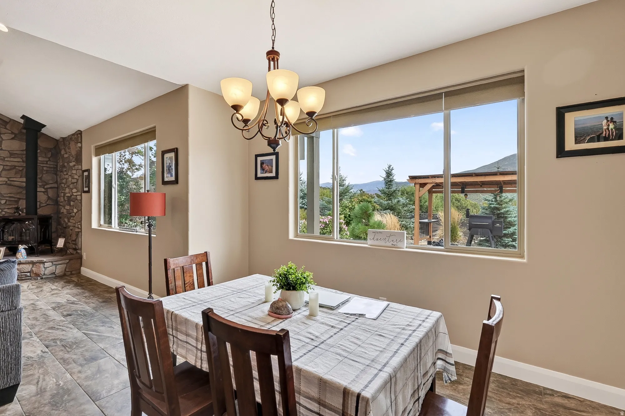 Bright dining area showcasing a pendant chandelier, tile flooring, and expansive windows framing mountain and tree-lined scenery