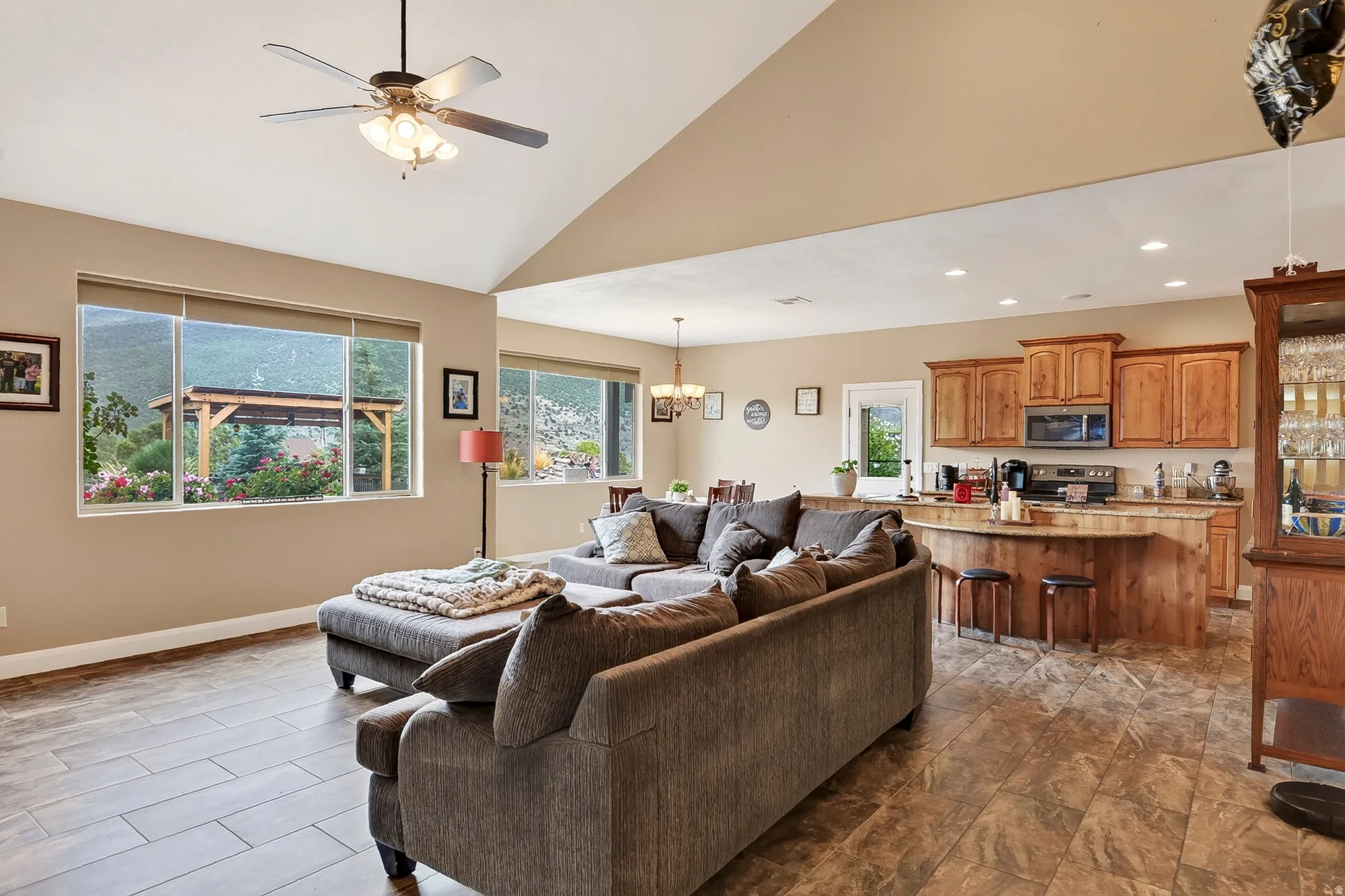 Open-concept living space with vaulted ceilings, ceiling fan with integrated lighting, and expansive windows offering natural light