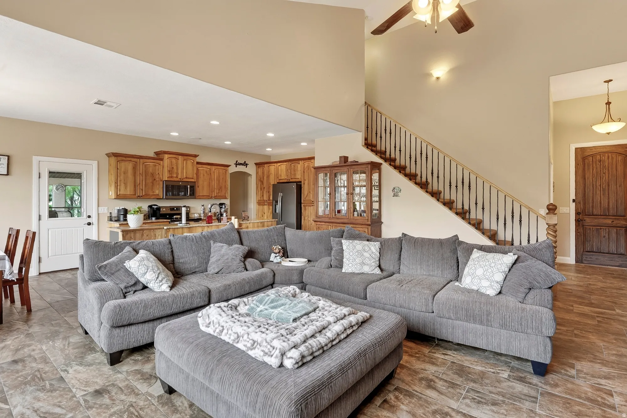 Open-concept living area featuring a sectional arrangement anchored by a wood-finish plank floor, recessed ceiling lighting, and direct sightlines to the kitchen