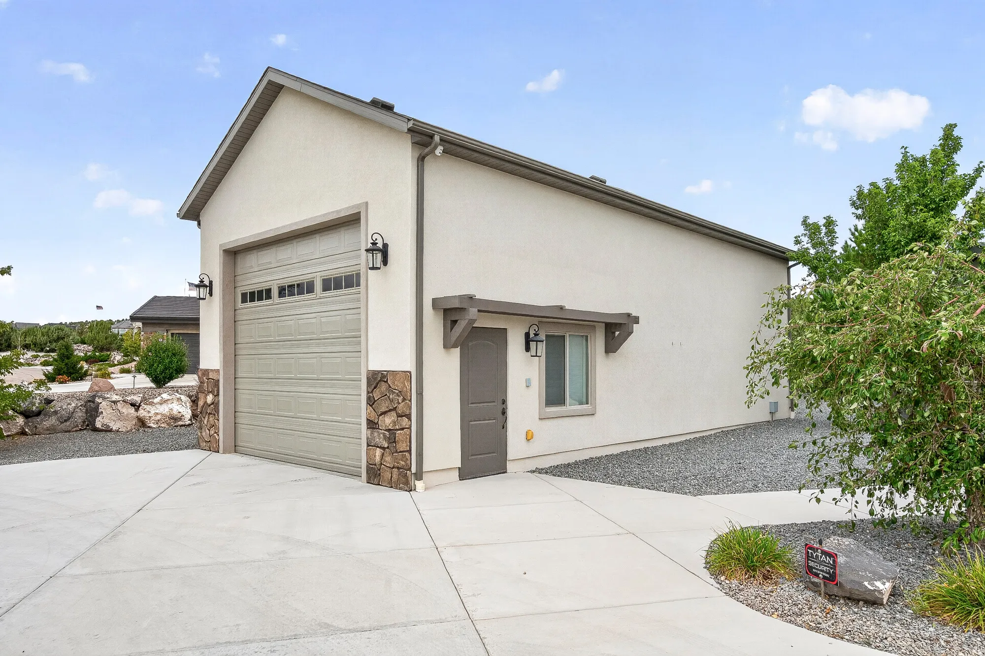 Modern single-story residence featuring a clean stucco exterior, attached garage with paneled overhead door, concrete driveway, and xeriscaped landscaping with decorative stone and mature shrubs