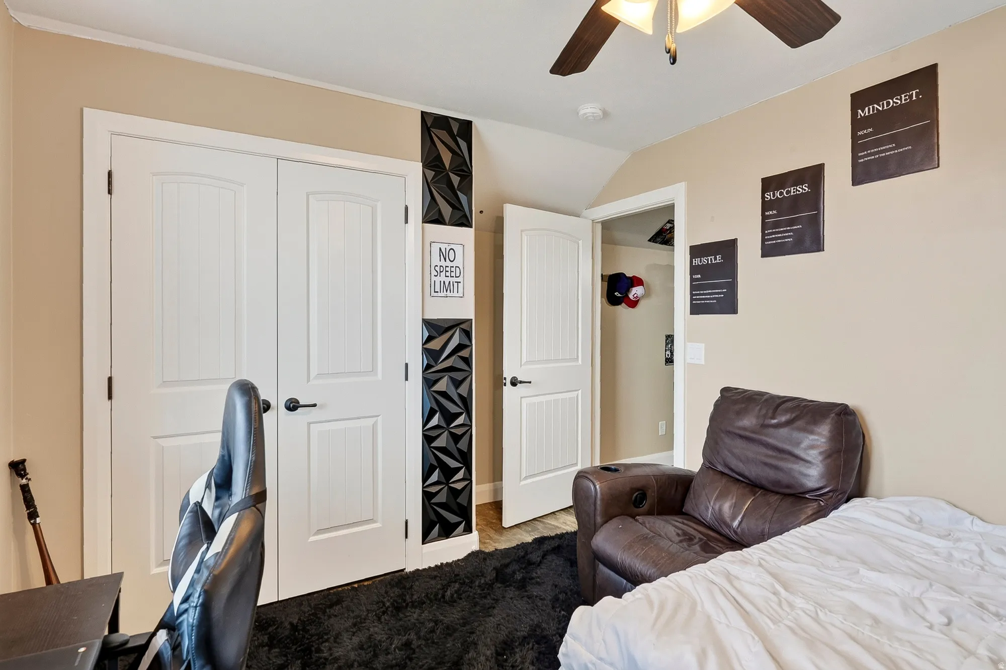 Spacious bedroom offering multiple closet options with six-panel white doors, ceiling fan with integrated lighting, warm neutral wall finishes, and dark wood-finish flooring throughout
