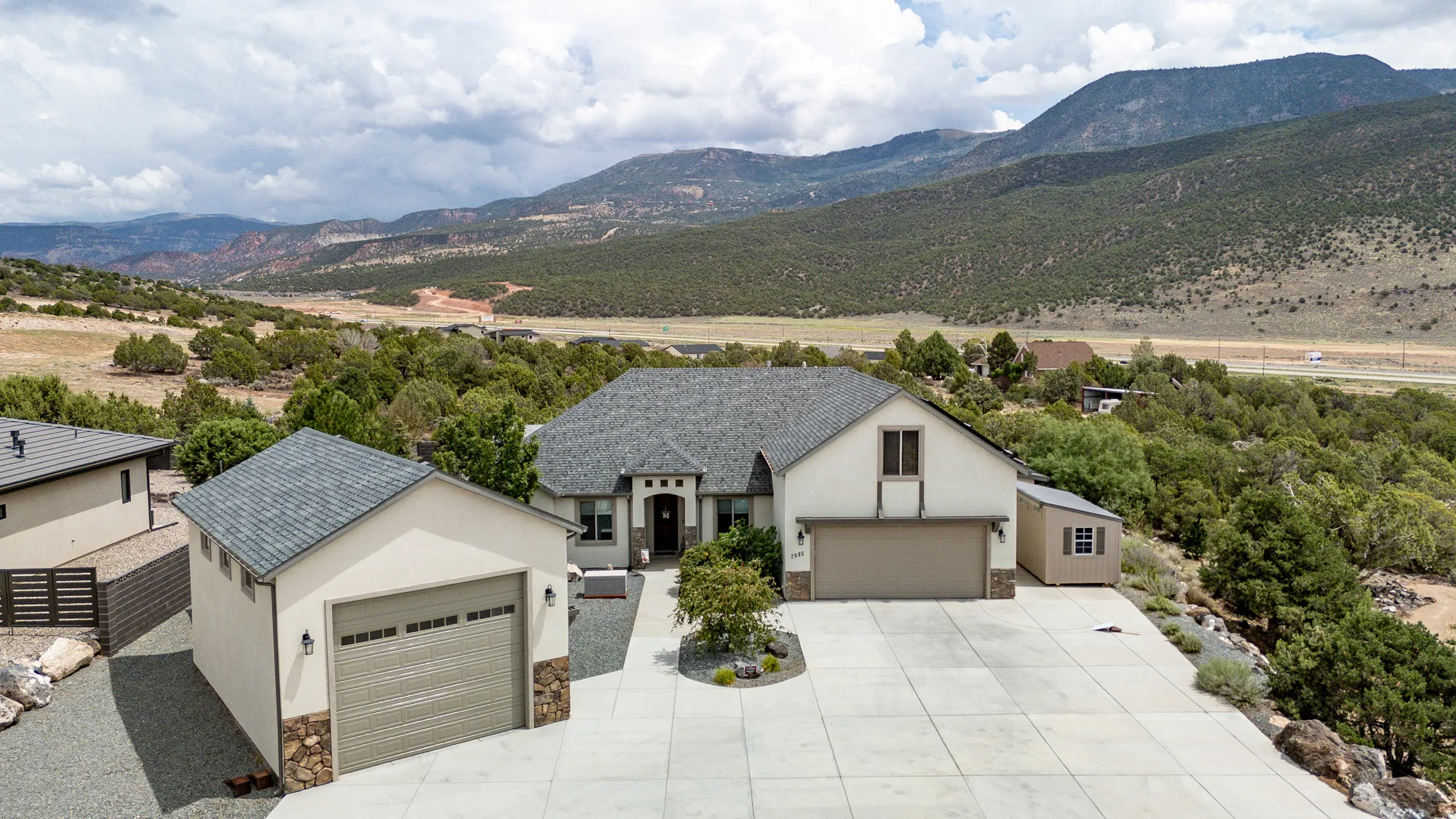 Modern residence showcasing a clean stucco exterior with peaked roofline, complemented by a three-car garage and additional detached garage structure