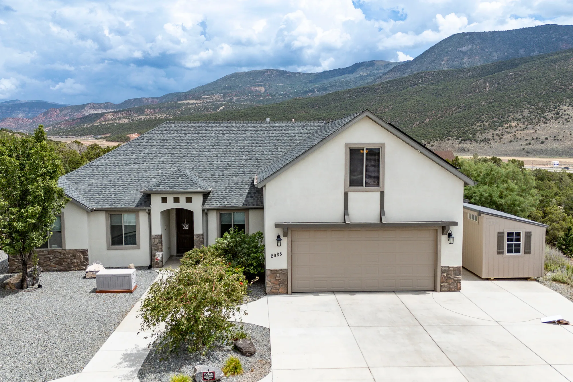 Modern single-story residence featuring a clean-lined stucco exterior with stone accents, pitched roofline with dimensional asphalt shingles, and a two-car attached garage with a neutral-finish door