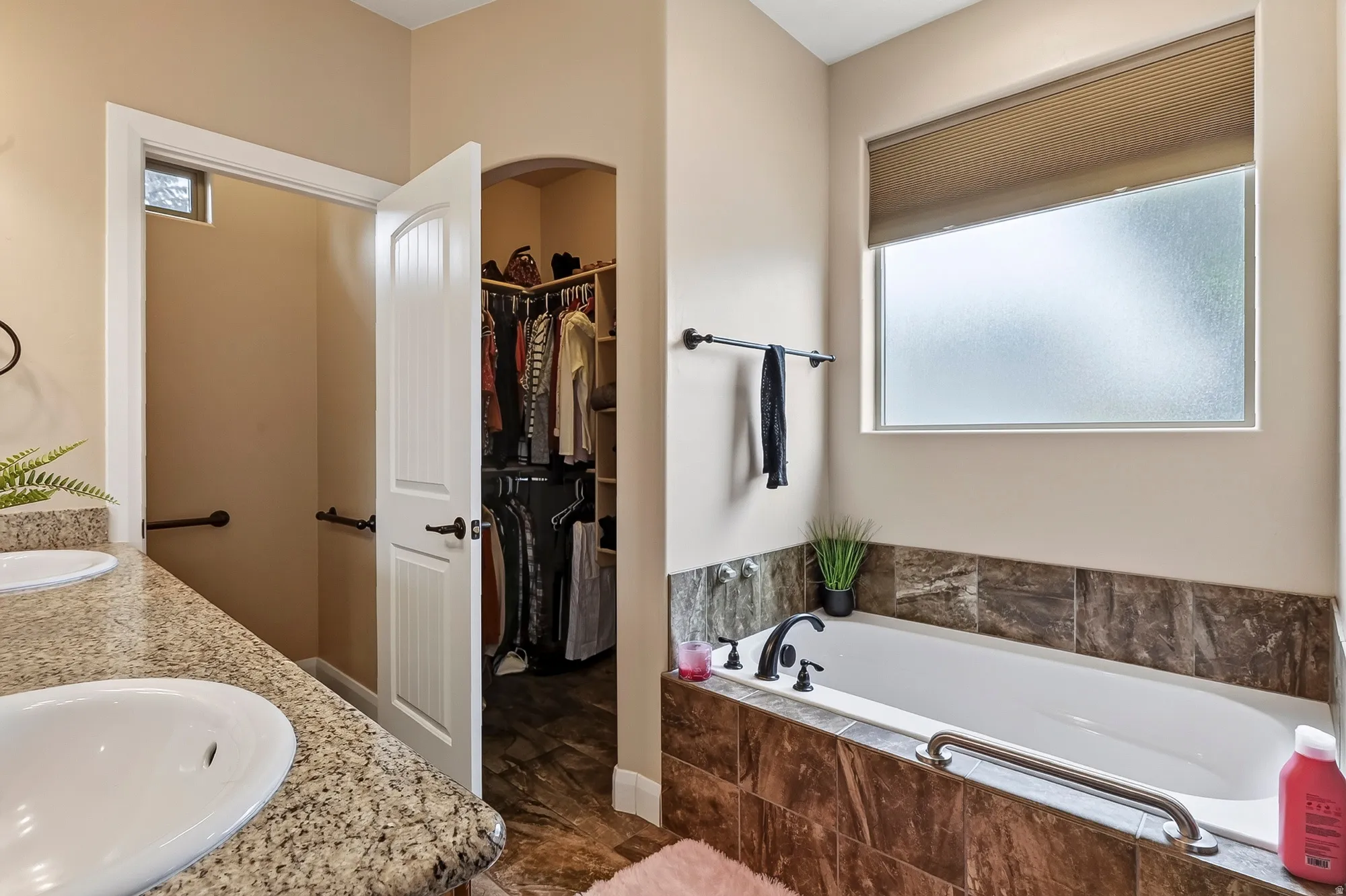 Primary Bathroom featuring a soaking tub with chrome fixtures, granite-finish wall surround, and a large window with frosted glass