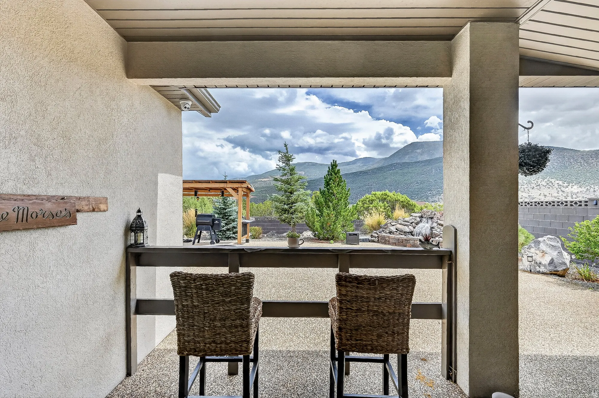 Covered outdoor entertaining space featuring a woven-seat bar with black metal framing, concrete flooring, and structural concrete columns