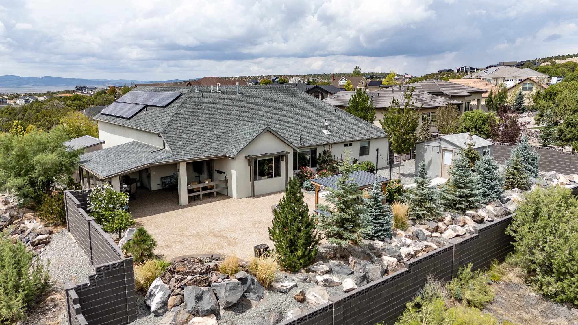 Modern residence showcasing a composite shingle roof, professional landscaping with mature evergreens and decorative stone hardscaping, a three-car attached garage with covered entry, and expansive concrete driveway