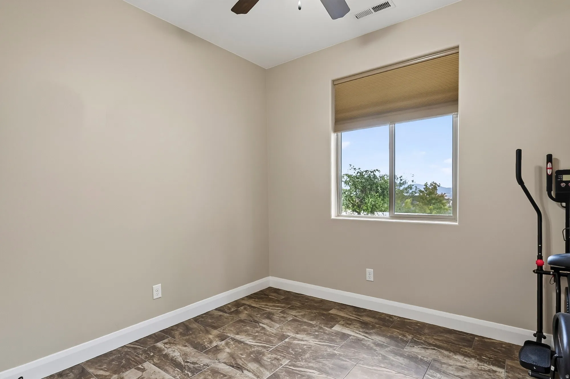 Bright secondary bedroom with large window framing natural light, neutral wall finish, wood-finish plank flooring, and white trim detail throughout
