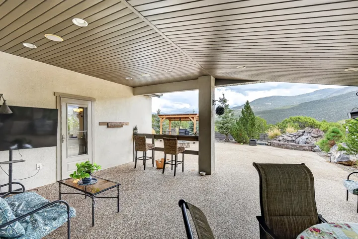 Covered outdoor living space featuring corrugated metal ceiling with recessed lighting, polished concrete flooring, and panoramic mountain vistas