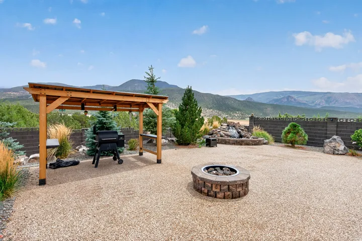 Expansive outdoor entertaining space featuring a wood-beam pergola, built-in fire pit with stone surround, and gravel hardscaping