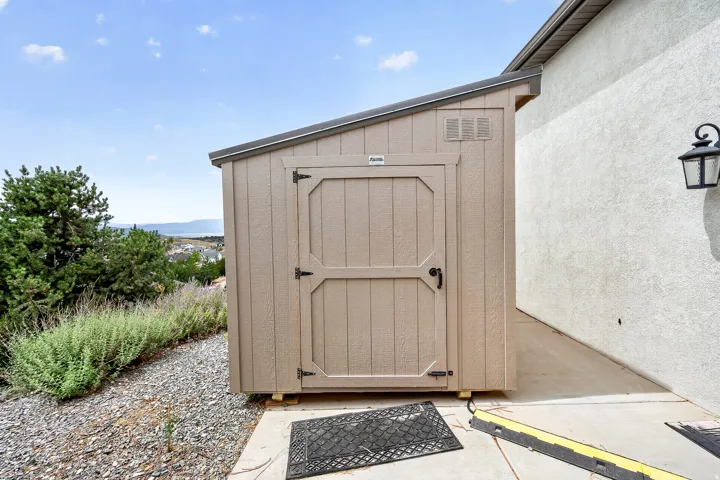 Exterior storage shed with a lean-to roof, situated on a concrete pad, adjacent to a stucco wall with an outdoor light fixture