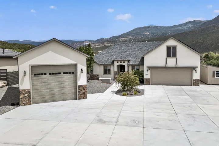 Modern residence showcasing a spacious concrete driveway with dual garage bays, crisp white exterior with peaked rooflines, and mountain backdrop