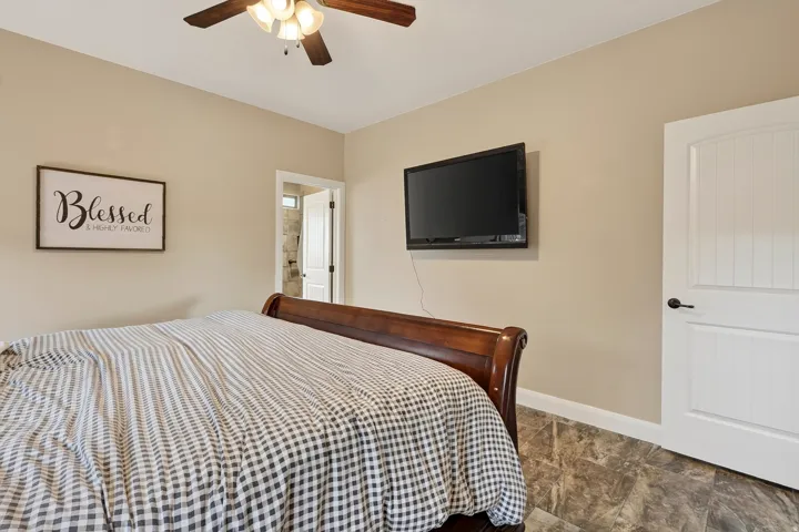 Primary bedroom featuring a wood-finish sleigh bed, ceiling fan with integrated lighting, wall-mounted flat-screen television, and neutral beige walls