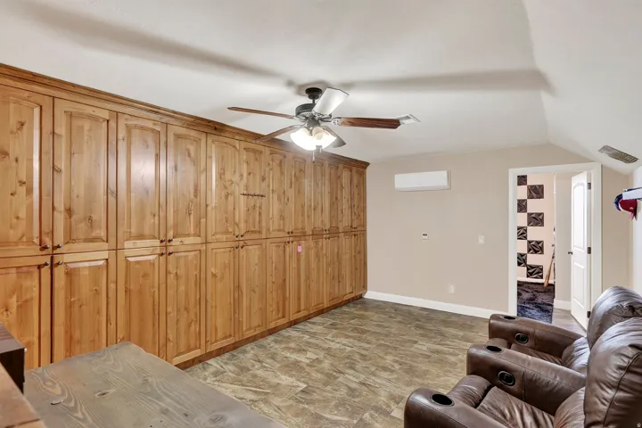 Spacious primary suite featuring extensive wood cabinetry with vertical paneling, ceiling fan with integrated lighting, and neutral carpeting throughout