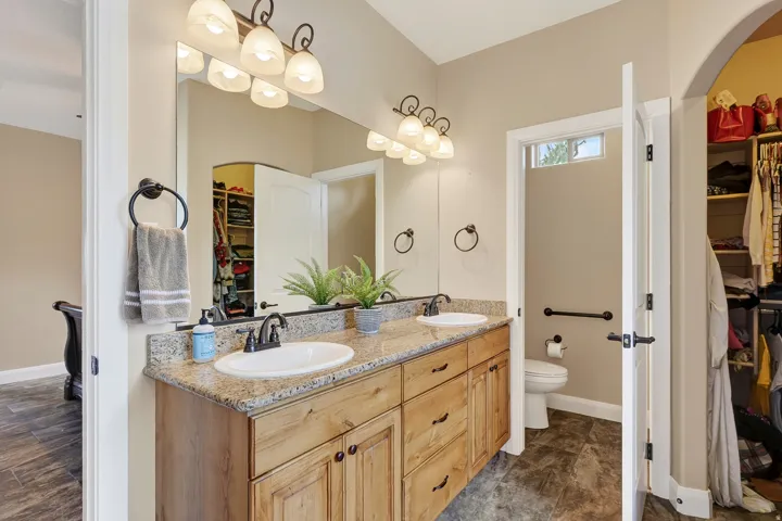 Spa-inspired primary bathroom featuring dual vanities with wood cabinetry, stone-finish countertops, and oil-rubbed bronze hardware