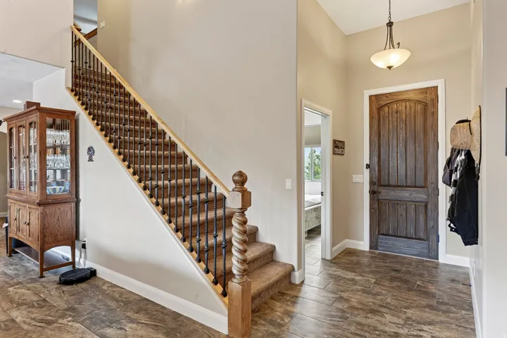 Welcoming foyer showcasing a grand wooden staircase with turned balusters and newel posts, wide-plank wood-finish flooring, and a pendant light fixture