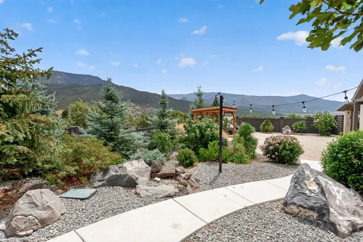 Professionally landscaped outdoor living space featuring a concrete pathway, river rock hardscaping, mature evergreen plantings, and a wooden pergola structure
