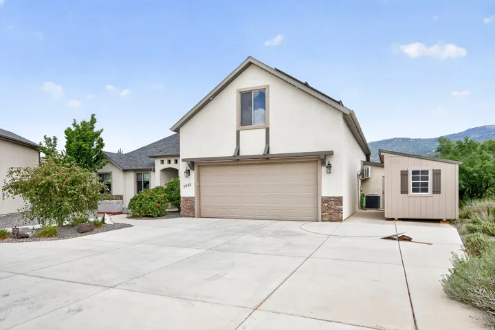 Stucco exterior with stone accents, attached two-car garage, concrete driveway, and a detached shed with a window