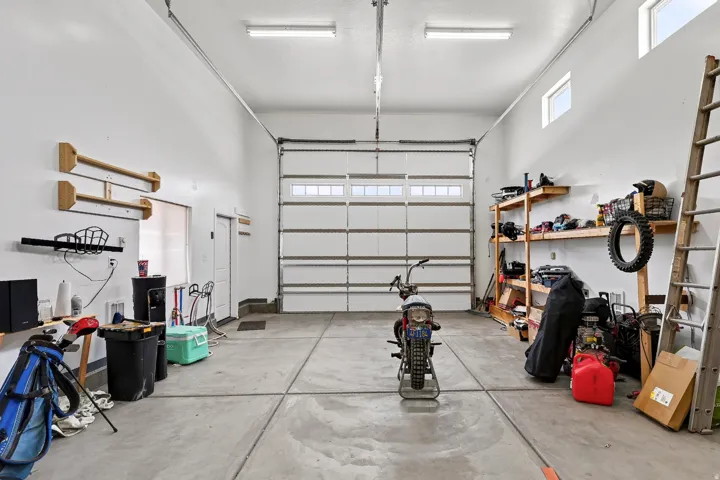 Spacious garage with concrete flooring, overhead fluorescent lighting, and a white paneled garage door with upper window inserts