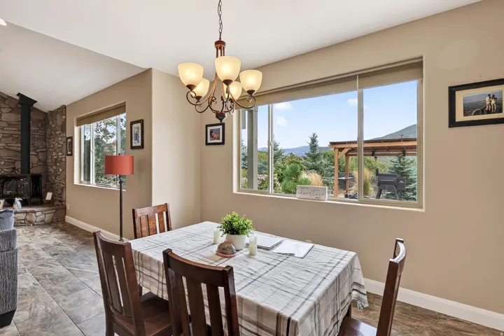 Bright dining area showcasing a pendant chandelier, tile flooring, and expansive windows framing mountain and tree-lined scenery