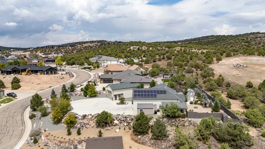 Modern residential architecture showcasing solar panel installation, contemporary geometric design with clean lines, expansive hardscaped grounds with mature landscaping, hillside setting with panoramic vistas, and thoughtfully positioned specimen trees t