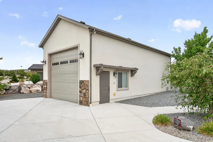 Modern single-story residence featuring a clean stucco exterior, attached garage with paneled overhead door, concrete driveway, and xeriscaped landscaping with decorative stone and mature shrubs