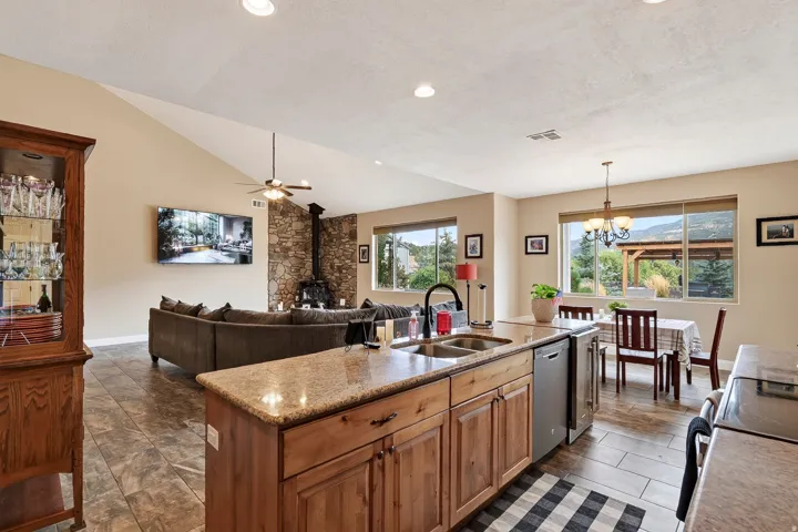 Open-concept kitchen and living area featuring custom wood cabinetry with granite countertops, stainless steel appliances, recessed lighting, and large multi-pane windows overlooking the landscape
