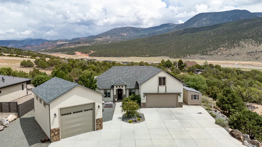 Modern residence showcasing a clean stucco exterior with peaked roofline, complemented by a three-car garage and additional detached garage structure