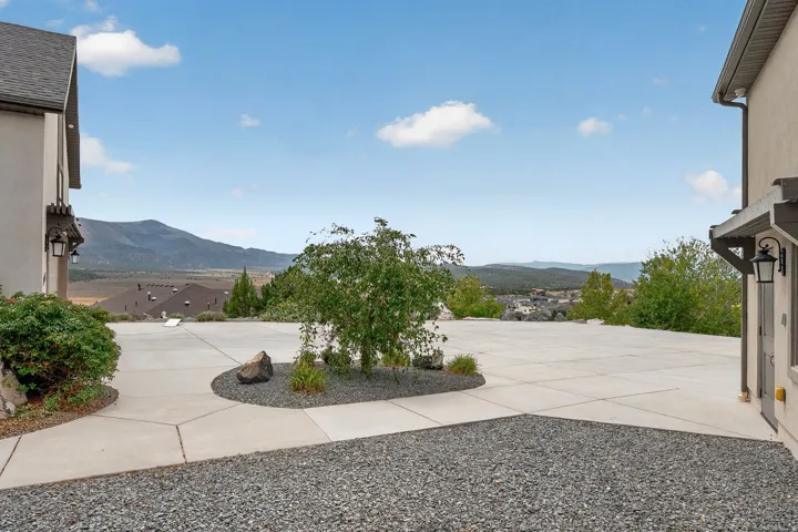 Expansive concrete patio with integrated gravel planting beds and mature landscaping, framed by mountain vistas and flanked by contemporary residential architecture on both sides
