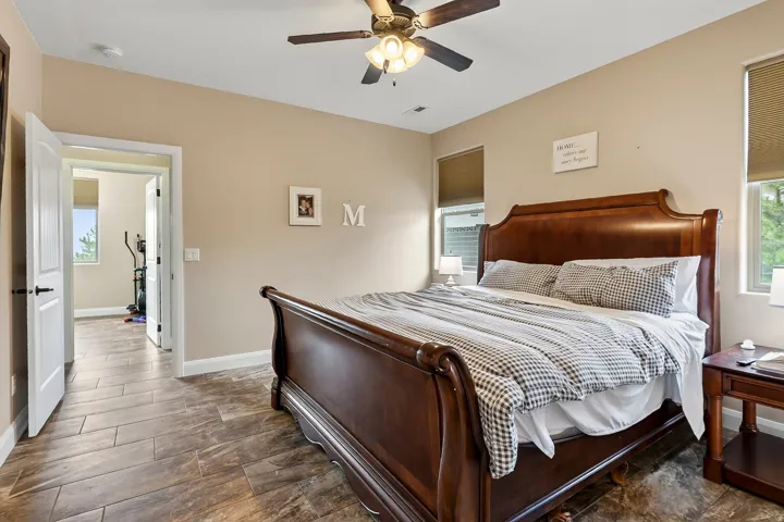 Master bedroom featuring a wood-finish sleigh bed, neutral wall tones, ceiling fan with integrated lighting, tile flooring, and abundant natural light from dual windows