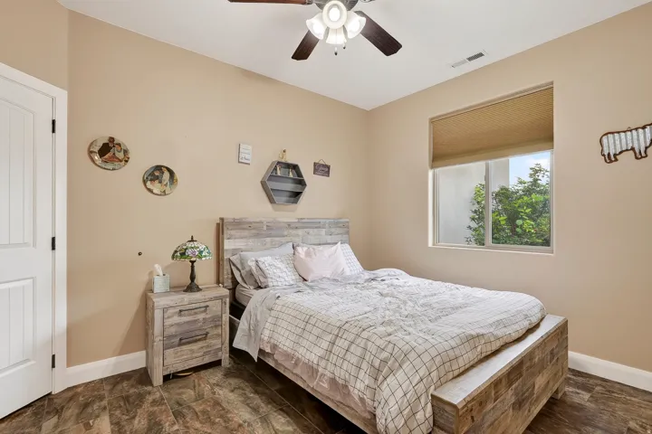 Spacious bedroom featuring a wood-finish bed frame with storage drawer base, coordinating wood-finish nightstand, ceiling fan with integrated lighting, and large picture window with cellular shade