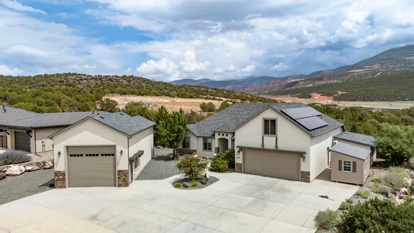 Stucco exterior with stone accents, attached garage, detached garage, solar panels, and mountain scenery