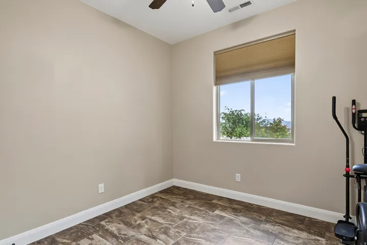 Bright secondary bedroom with large window framing natural light, neutral wall finish, wood-finish plank flooring, and white trim detail throughout