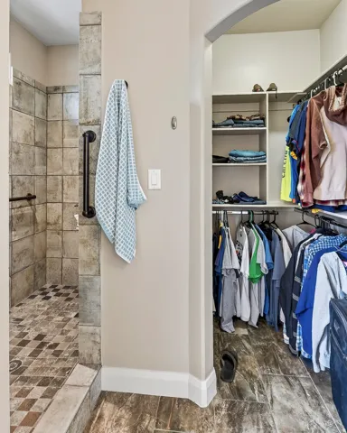 Tiled walk-in shower with grab bars, integrated shelving, and a built-in closet system