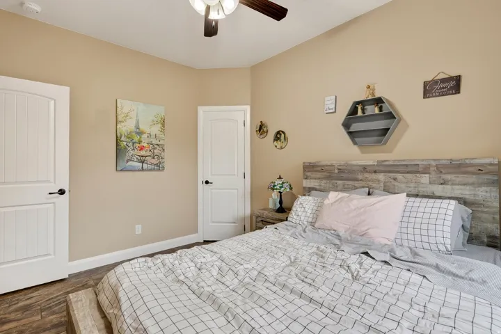 Master bedroom featuring a wood-finish accent headboard wall, ceiling fan with integrated lighting, plush bedding, two white six-panel closet doors, and warm neutral wall finishes throughout