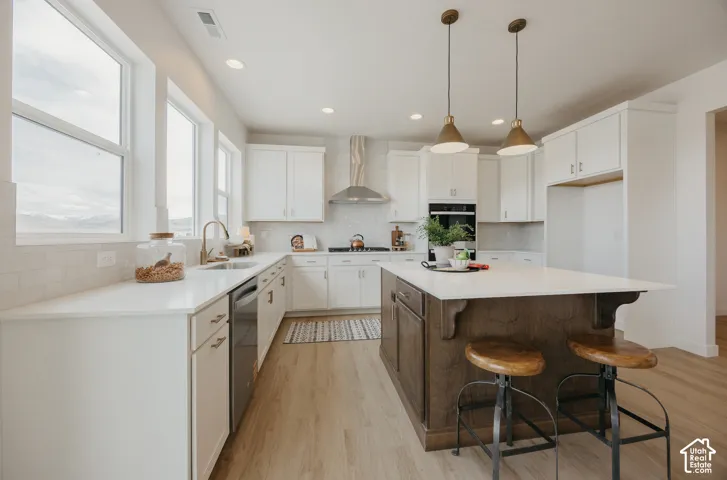 Kitchen featuring white cabinetry, light-toned wood-finish flooring, a central island with a contrasting wood finish, white countertops, and stainless steel appliances