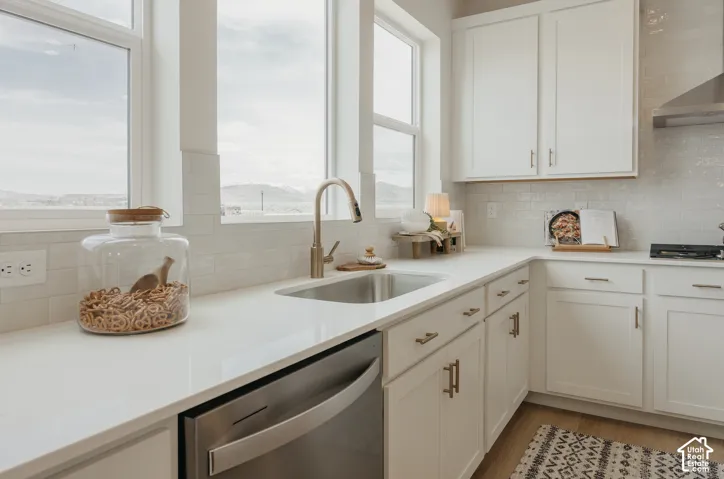 White shaker-style cabinetry, stainless steel sink with a gooseneck faucet, light-toned countertops, and a white subway tile backsplash