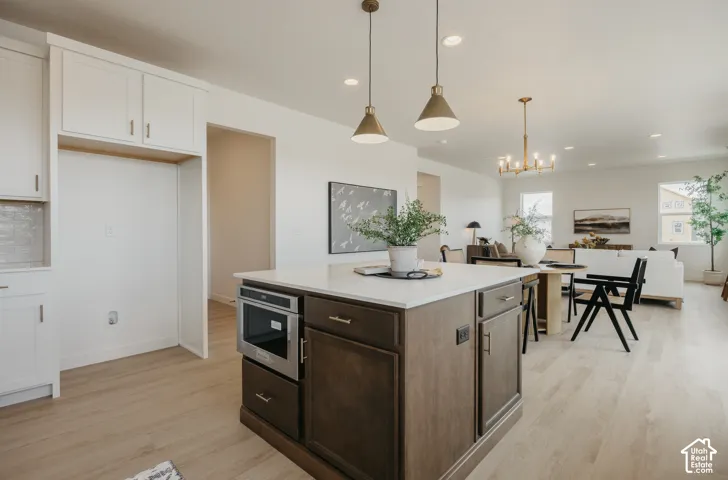 Kitchen island with built-in microwave, light-toned wood-finish flooring, white cabinetry, recessed lighting, and pendant light fixtures