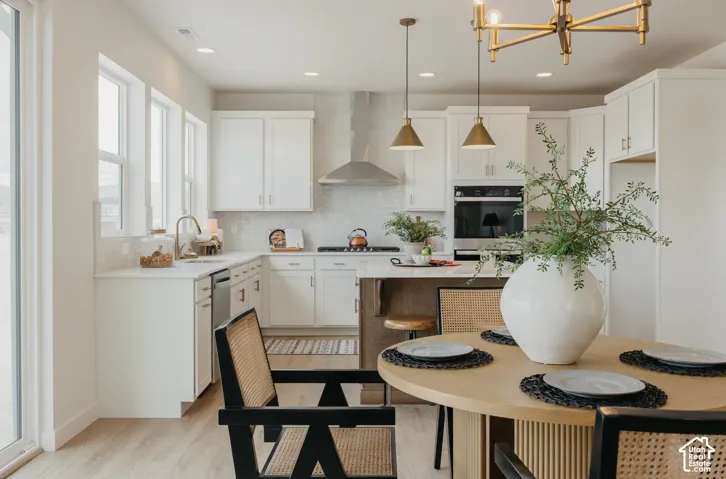 White cabinetry, stainless steel appliances, wood-finish flooring, recessed lighting, and a contemporary chandelier