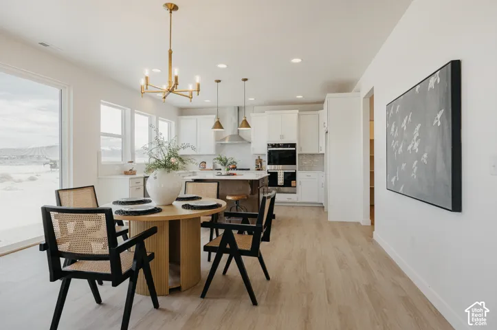 Open-concept living area with light wood-finish flooring, a contemporary brass chandelier, white cabinetry, integrated double ovens, and a kitchen island with seating