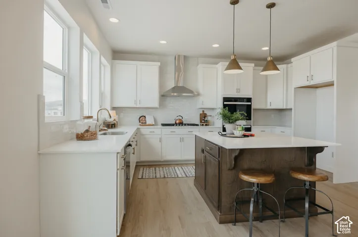 White cabinetry with brushed brass hardware, light wood-finish flooring, white countertop, white tile backsplash, and a dark wood kitchen island
