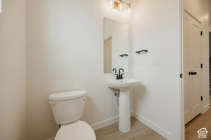 Pedestal sink with a matte black faucet, wall-mounted mirror, and wood-finish flooring